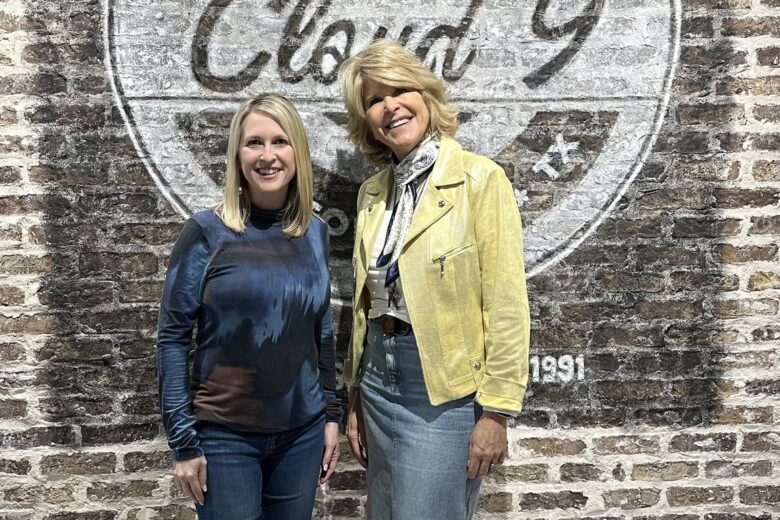 Stephanie Wilson and Kim Cloud inside Cloud 9 Salon and Spa in front of the Cloud 9 logo on a dark brick wall.